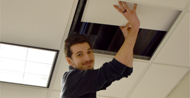 building services assistant fixing the ceiling on a ladder